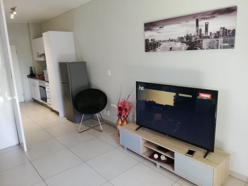 Open-plan living area featuring tiled flooring and a compact, modern kitchen with built-in cabinetry and integrated appliances.