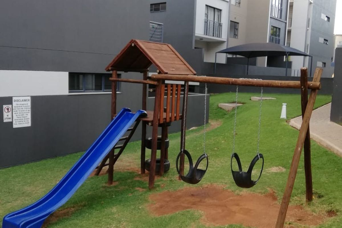 A communal outdoor area featuring a children's playground set situated between modern multi-story apartment buildings with paved walkways.