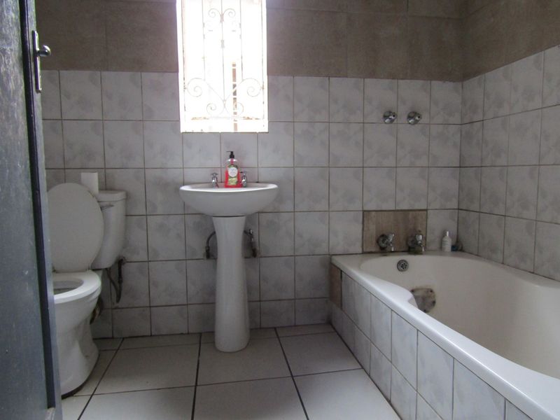 A functional bathroom featuring a pedestal basin, toilet, and built-in bathtub with tiled finishes throughout.