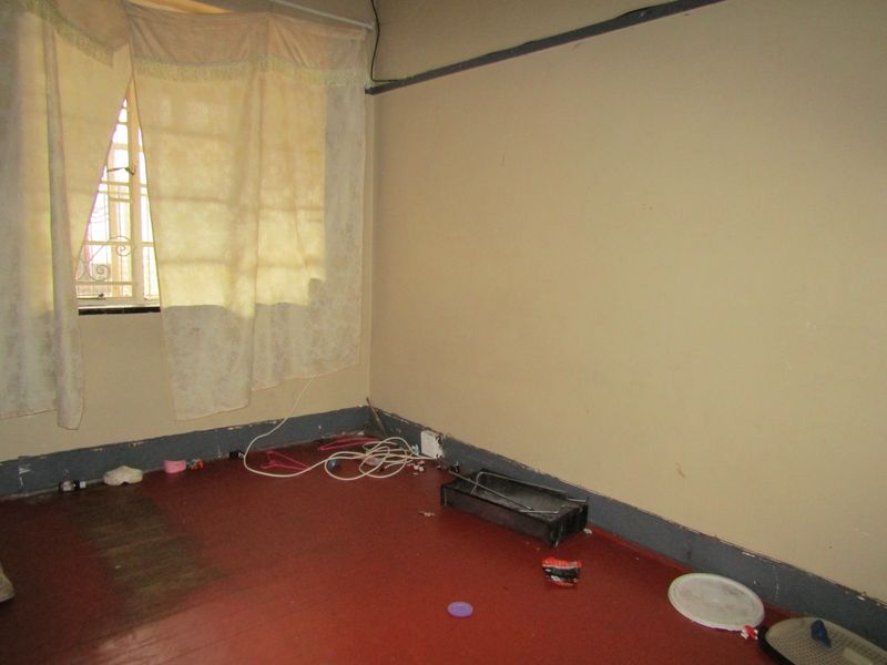 A vacant bedroom featuring security bars on the window and worn flooring, requiring cosmetic updates to improve its overall condition and appeal.
