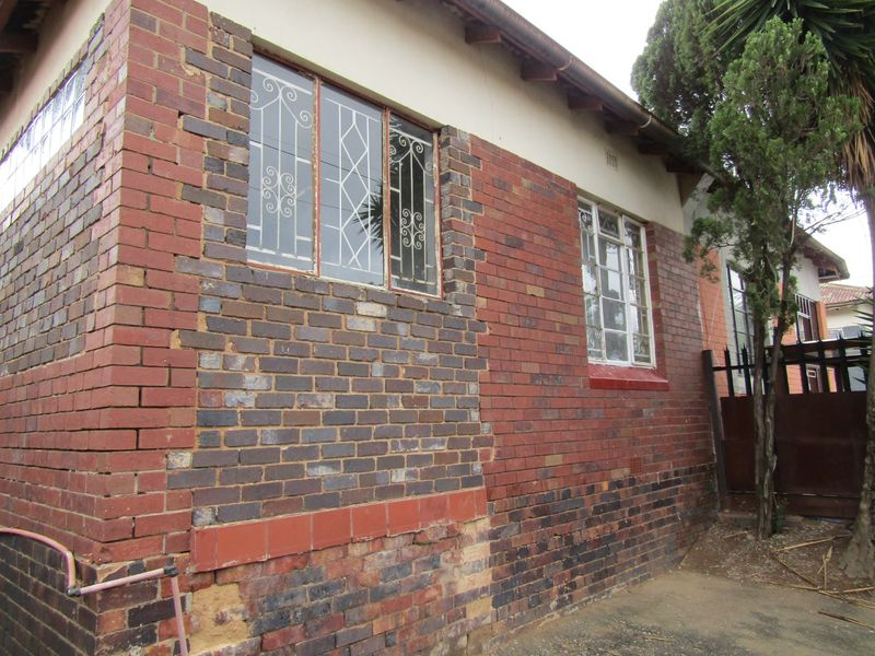 Exterior view of the property showing face brick walls with security bars on steel windows and visible signs of masonry wear.