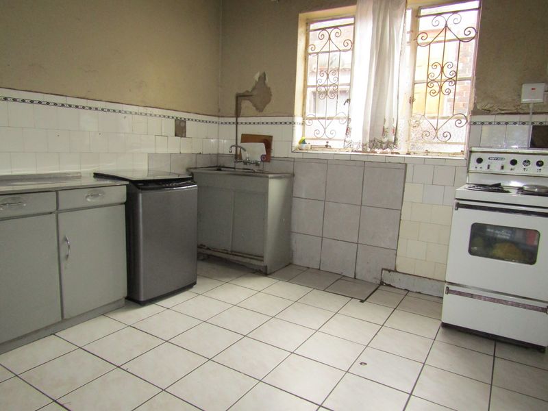 A dated kitchen featuring tiled flooring, a stainless steel sink, and a freestanding stove, requiring significant cosmetic updates and wall repairs.