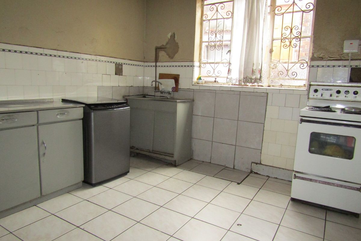 A dated kitchen featuring tiled flooring, a stainless steel sink, and a freestanding stove, requiring significant cosmetic updates and wall repairs.