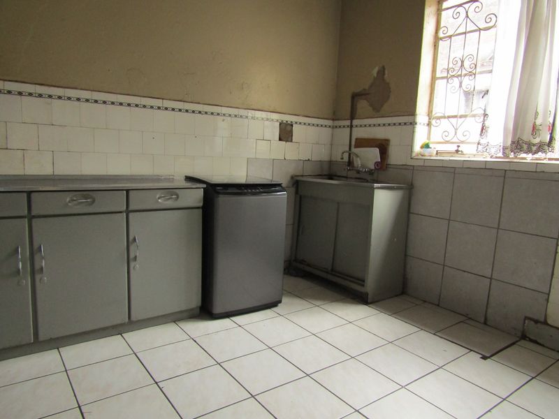 A functional laundry area featuring tiled splashbacks, a metal sink unit, and security bars on the window, requiring cosmetic updates to wall finishes.