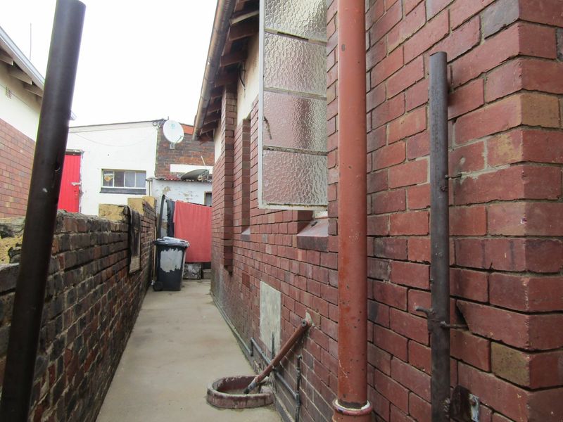 A narrow side passage featuring exposed brick walls, concrete flooring, and external plumbing fixtures along the side of the house.