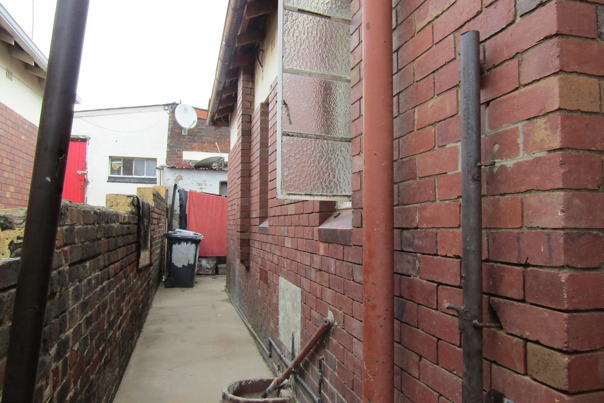 A narrow side passage featuring exposed brick walls, concrete flooring, and external plumbing fixtures along the side of the house.