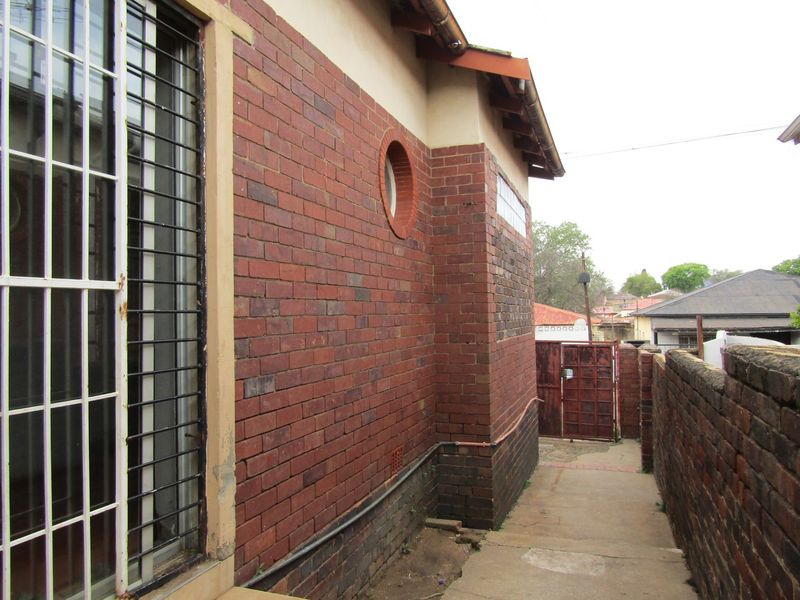 Side exterior view of the property featuring face brick walls, a circular window, security bars, and a concrete pathway leading to a rear gate.