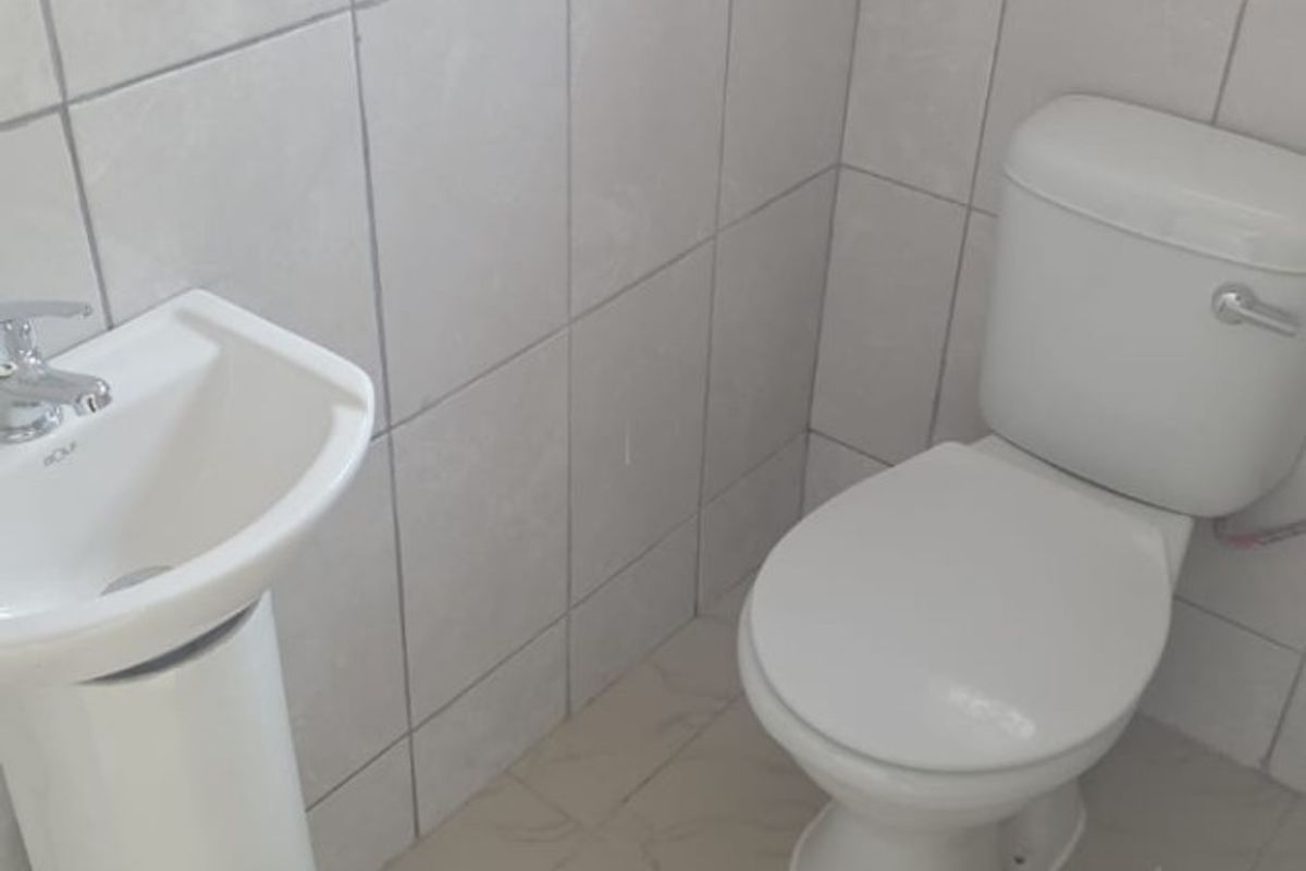 A compact bathroom featuring a pedestal basin and a standard toilet with neutral wall and floor tiling.