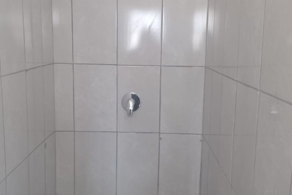 A functional shower enclosure featuring neutral wall and floor tiling with a modern chrome shower head and mixer tap.
