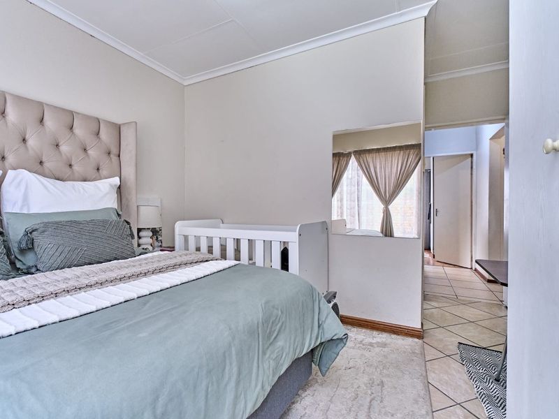 A bedroom featuring tiled flooring and a wall-mounted mirror, with direct access to an adjoining hallway.