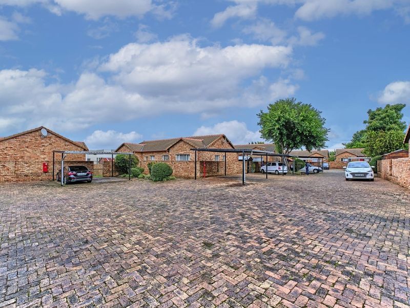 A view of the townhouse complex exterior featuring a large paved parking area with multiple carport structures and facebrick building facades.