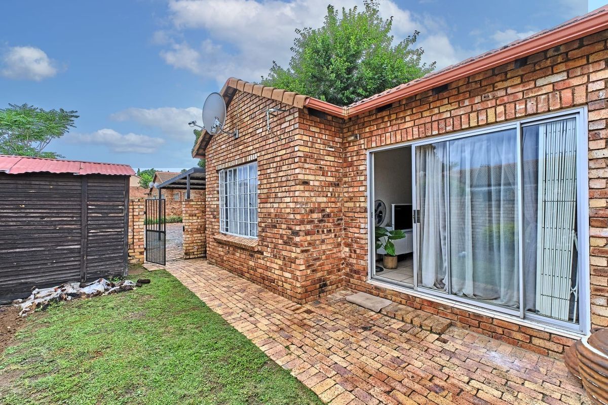 Rear view of the townhouse featuring face brick construction, a paved patio area, sliding glass doors, and a small garden space with a storage shed.
