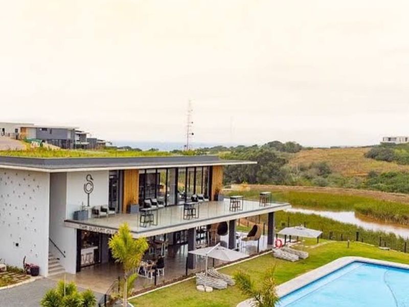 A modern clubhouse facility featuring a green roof, expansive covered patio, and an adjacent swimming pool overlooking a natural landscape.