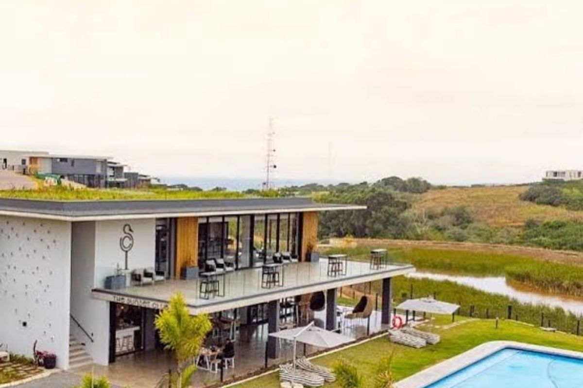 A modern clubhouse facility featuring a green roof, expansive covered patio, and an adjacent swimming pool overlooking a natural landscape.