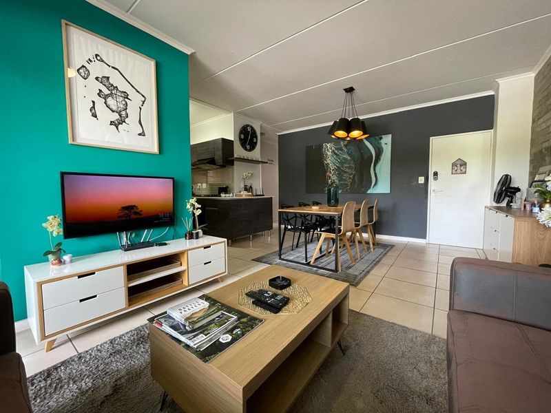 An open-plan living and dining area featuring tiled floors, modern pendant lighting, and a connected kitchen space with dark cabinetry.