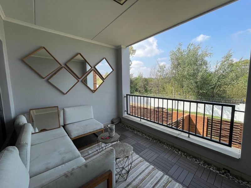 A covered balcony featuring tiled flooring and a metal balustrade, offering an open outdoor space with views of the surrounding greenery.