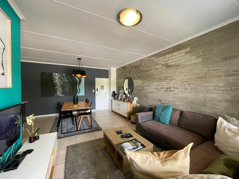 An open-plan living and dining area featuring a prominent exposed brick wall, tiled flooring, and a modern accent wall.