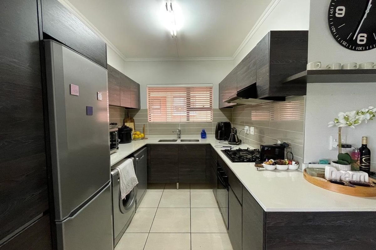 Modern kitchen featuring dark wood cabinetry, stone countertops, gas hob, built-in oven, and tiled flooring with a functional U-shaped layout.