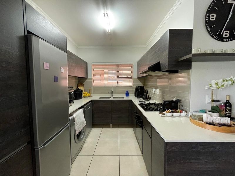 Modern kitchen featuring dark wood cabinetry, stone countertops, gas hob, built-in oven, and tiled flooring with a functional U-shaped layout.