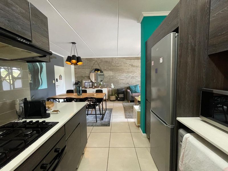 Open-plan living area featuring a modern kitchen with gas hob, stone countertops, and a striking exposed brick feature wall in the dining space.