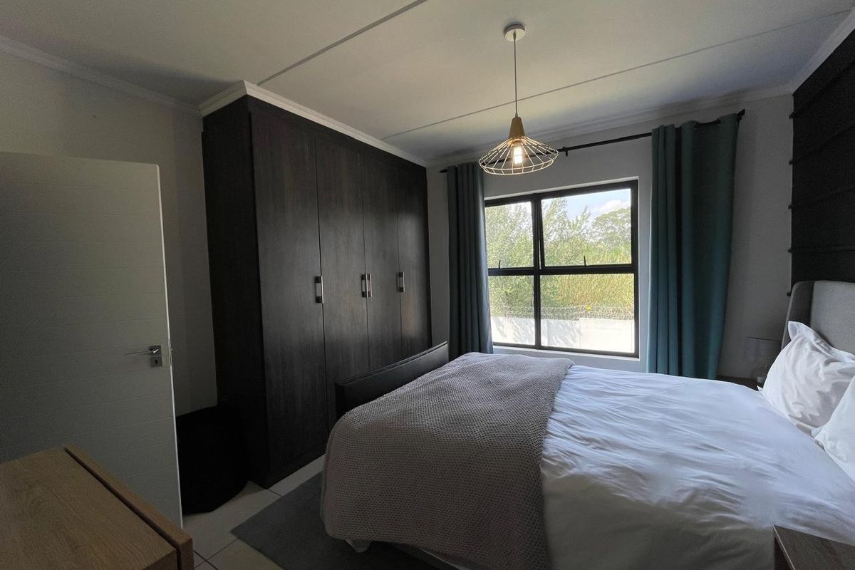 A well-maintained bedroom featuring dark wood built-in cupboards, tiled flooring, and a large window allowing for natural light.