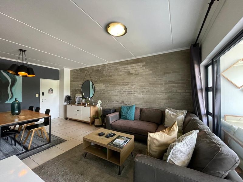 Spacious open-plan living and dining area featuring an exposed brick feature wall, tiled flooring, and large sliding glass doors providing natural light.