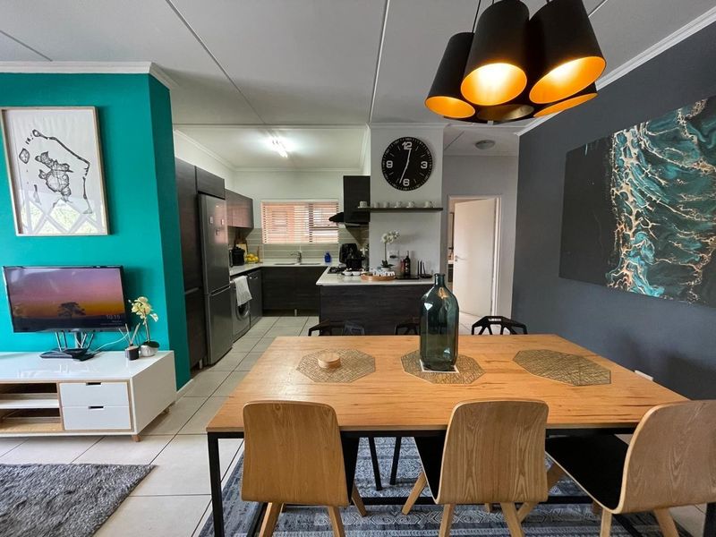 An open-plan living and dining area featuring a modern kitchen with dark cabinetry, a central island, and contemporary tiled flooring throughout.