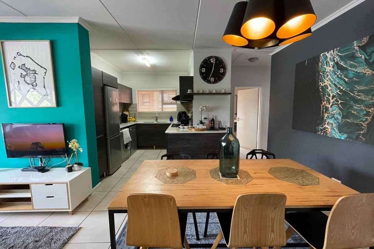 An open-plan living and dining area featuring a modern kitchen with dark cabinetry, a central island, and contemporary tiled flooring throughout.