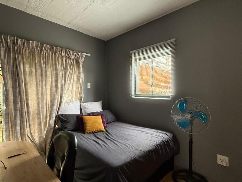 A bedroom featuring dark grey walls, a security gate leading to the exterior, and a window with venetian blinds.