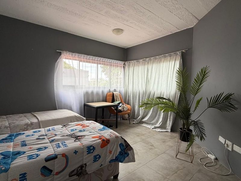 A bedroom featuring tiled flooring, textured ceilings, and large windows allowing natural light, providing a functional space for rest.
