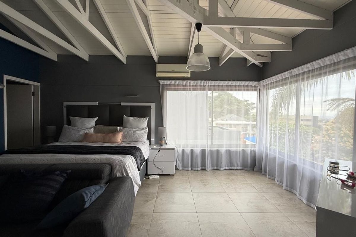 Spacious bedroom featuring exposed white timber rafters, tiled flooring, split-system air conditioning, and expansive corner windows providing ample natural light.
