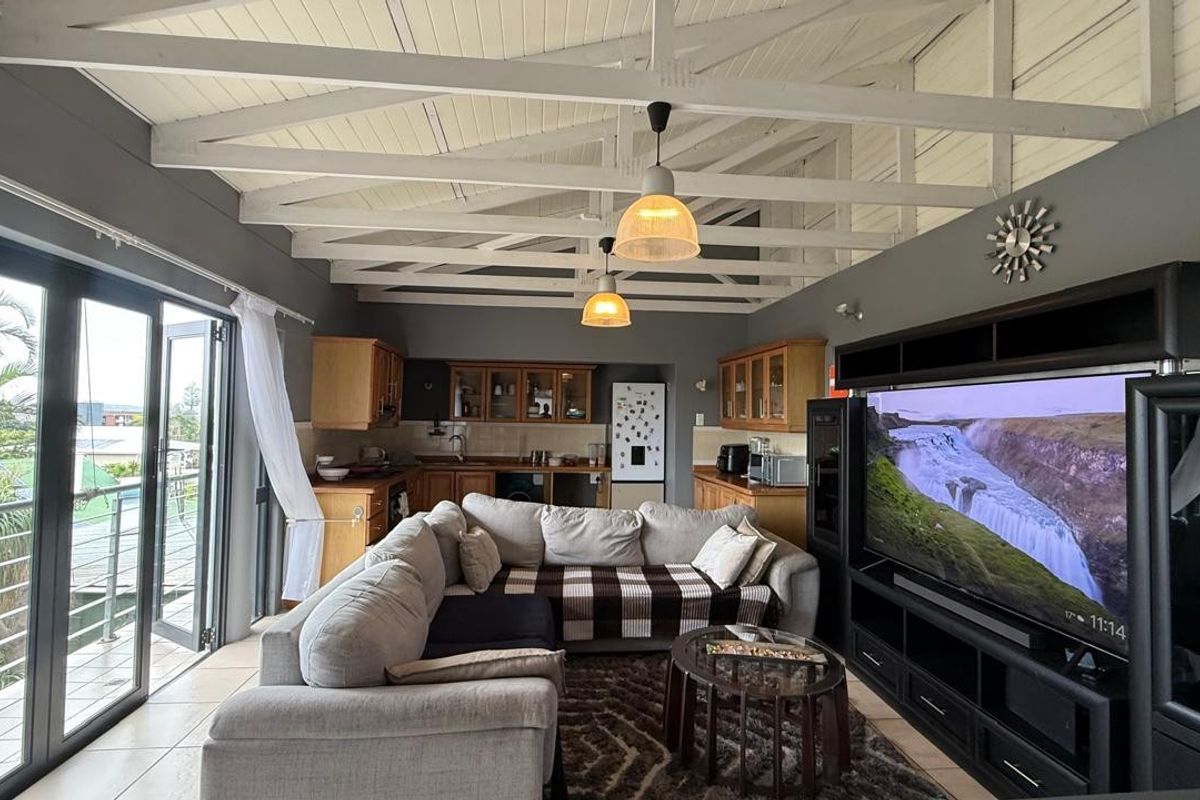 Spacious open-plan living and kitchen area featuring high exposed beam ceilings, tiled floors, and direct access to a balcony through large sliding glass doors.