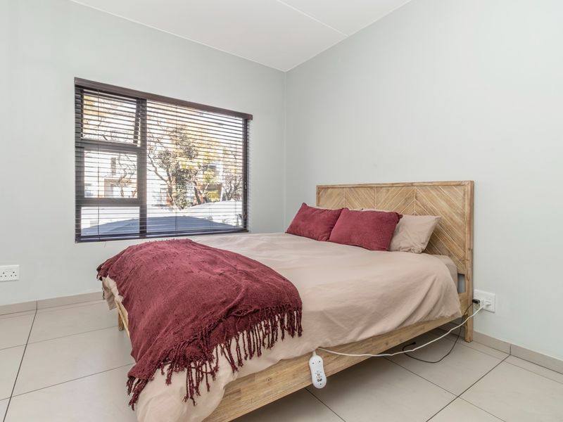 A bright and clean bedroom featuring neutral tiled flooring, light-colored walls, and a window fitted with venetian blinds.