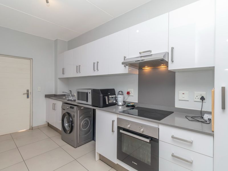 Modern kitchen featuring white high-gloss cabinetry, stone countertops, integrated oven, electric hob, extractor fan, and dedicated space for laundry appliances.
