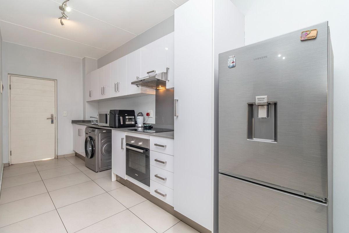 Modern kitchen featuring white cabinetry, integrated oven and hob, extractor fan, and tiled flooring with a dedicated laundry plumbing connection.