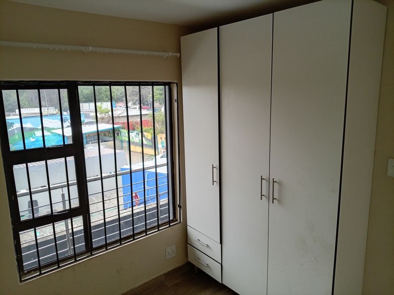 A bedroom featuring a built-in white wardrobe, tiled flooring, and a window fitted with security bars.