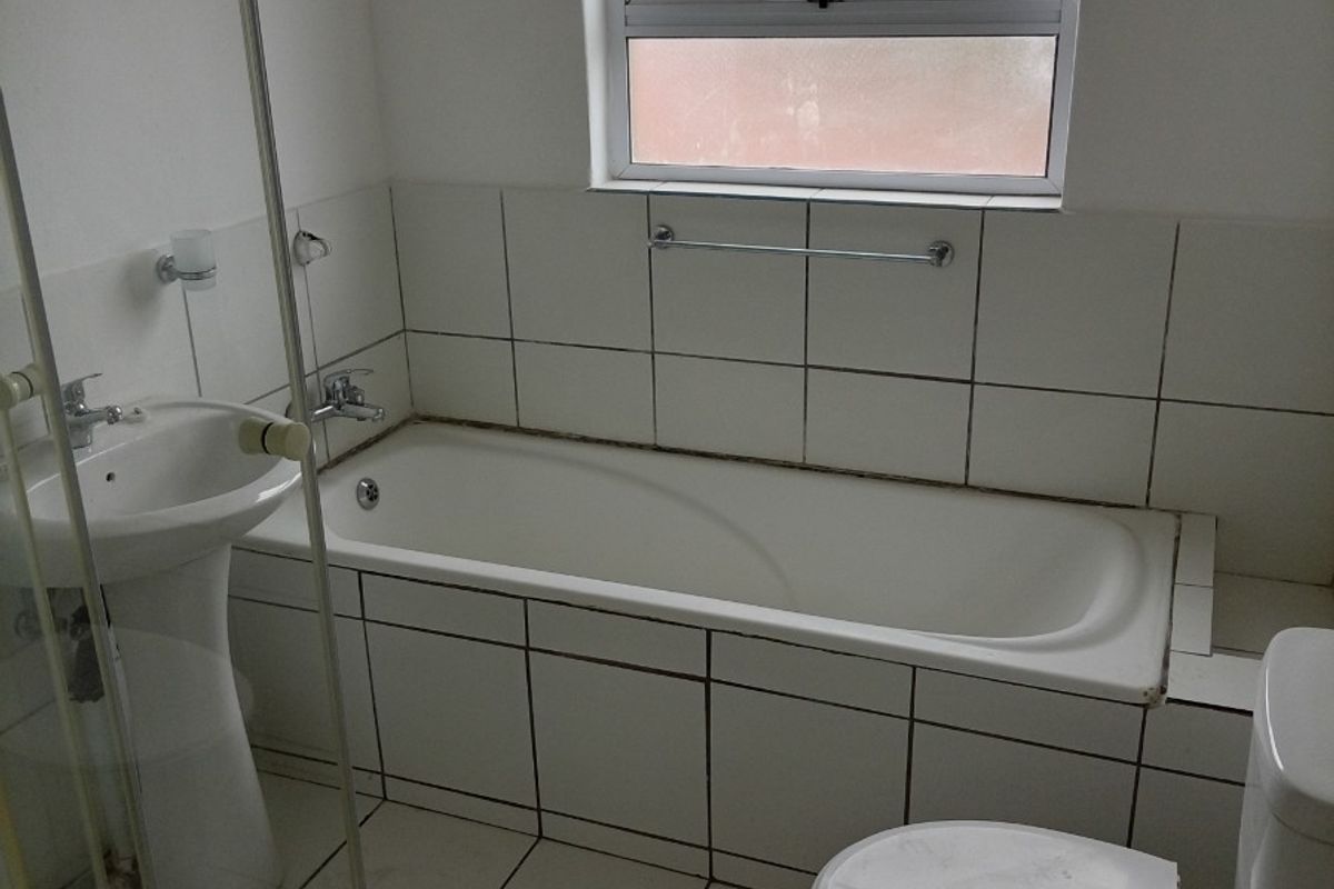 A functional bathroom featuring a pedestal basin, bathtub, separate shower enclosure, and tiled finishes throughout, offering a clean and practical layout.