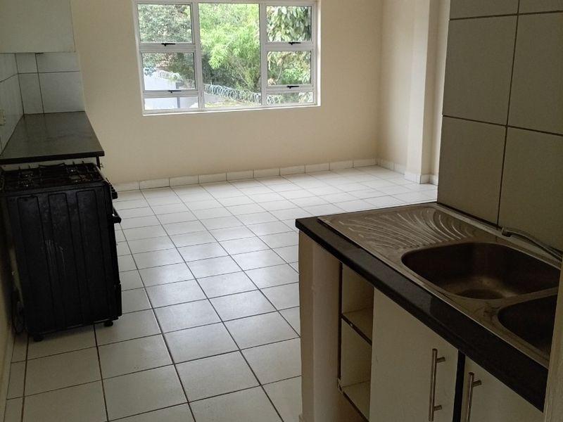An empty kitchen featuring tiled flooring, built-in cabinetry with a double bowl sink, and a gas stove, offering a functional layout for renovation.