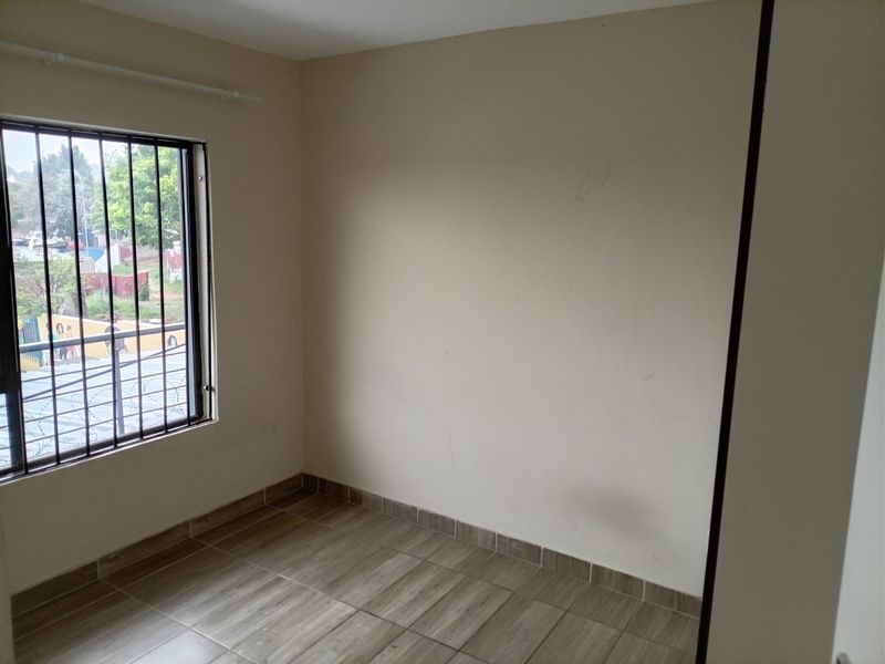 An empty bedroom featuring tiled flooring and a window fitted with security bars, presenting a blank canvas for personalization.