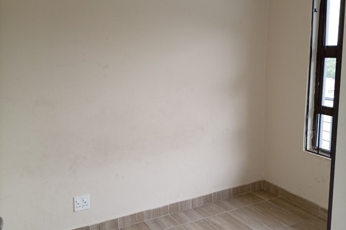 An empty bedroom featuring neutral tiled flooring, a single window with a curtain rail, and standard electrical outlets.
