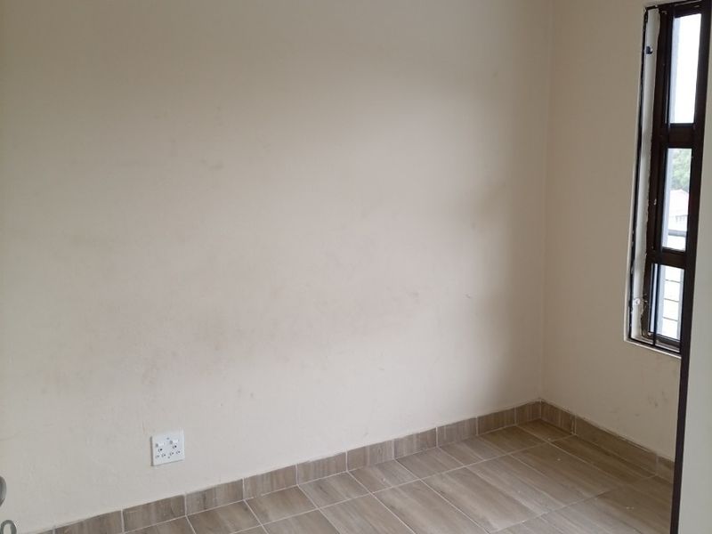 An empty bedroom featuring neutral tiled flooring, a single window with a curtain rail, and standard electrical outlets.