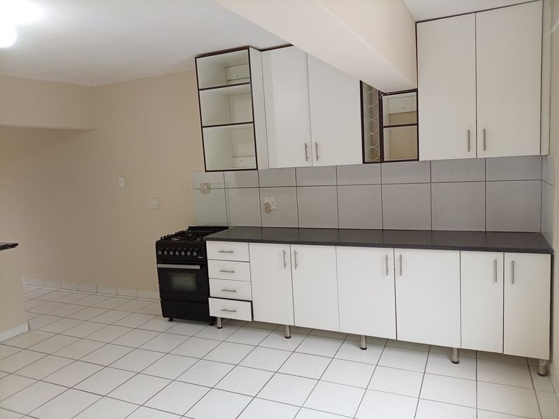 A functional kitchen featuring white built-in cabinetry, a tiled backsplash, dark laminate countertops, and a freestanding stove with tiled flooring throughout.