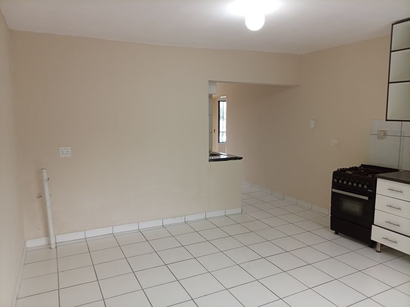 An empty kitchen area featuring tiled flooring, a freestanding stove, and basic cabinetry, with an open-plan layout leading to an adjacent space.