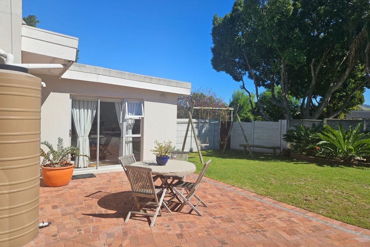 Rear exterior view featuring a brick paved patio, sliding door access to the home, a water tank, and a private garden with boundary walling.