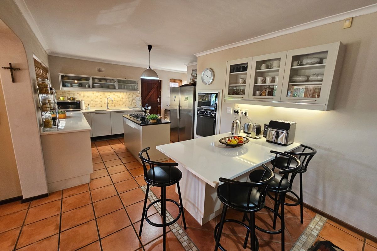 Spacious kitchen featuring modern cabinetry, stone countertops, a central island with breakfast bar seating, and integrated appliances, finished with durable tiled flooring.