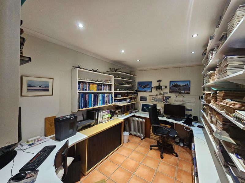 A functional home office featuring built-in desk space, extensive wall-mounted shelving, recessed lighting, and durable tiled flooring.