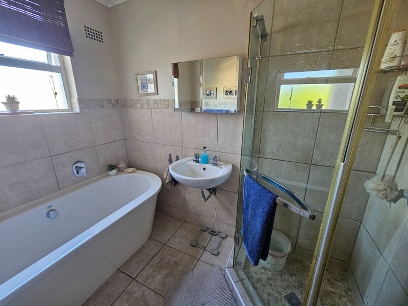A functional bathroom featuring a bathtub, wall-mounted basin, and a separate glass-enclosed shower with neutral wall and floor tiling.