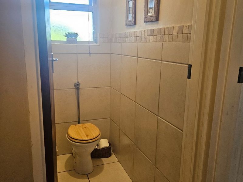 A compact guest bathroom featuring neutral ceramic wall and floor tiles with a decorative mosaic border and a window for natural light.