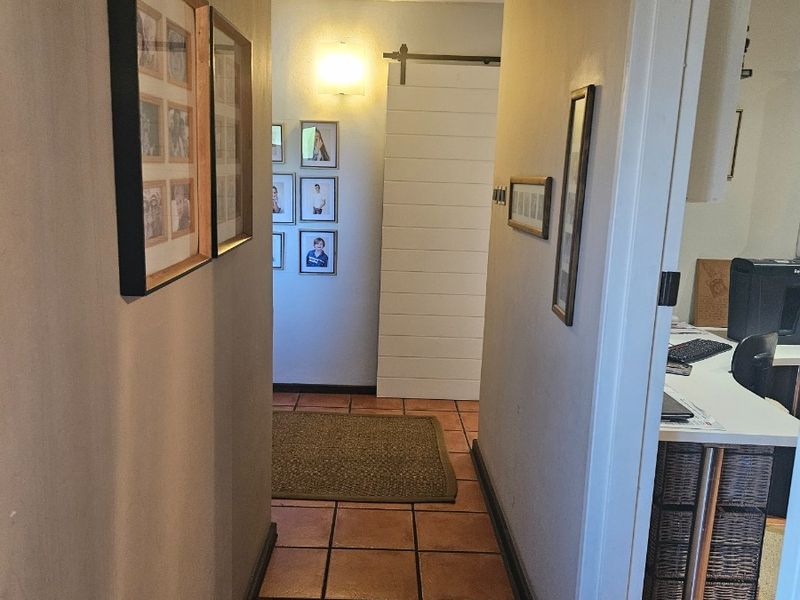 A functional hallway featuring terracotta floor tiles, a sliding barn-style door, and wall-mounted lighting, providing access to adjacent rooms.