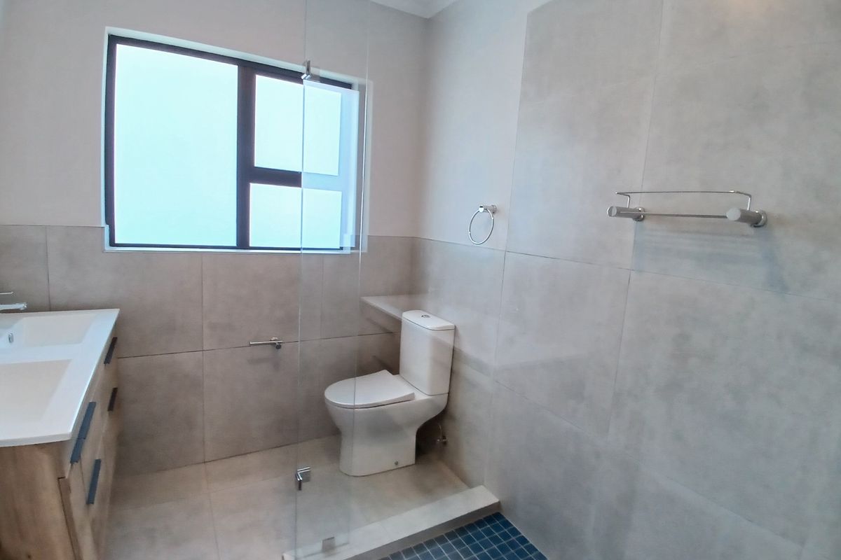Modern bathroom featuring a double vanity, toilet, and a walk-in shower with a glass screen and tiled finishes.